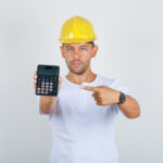 Safety Gear ROI Calculator: How Much Does Safety Infrastructure Save? Builder man pointing finger at calculator in white t-shirt, helm
